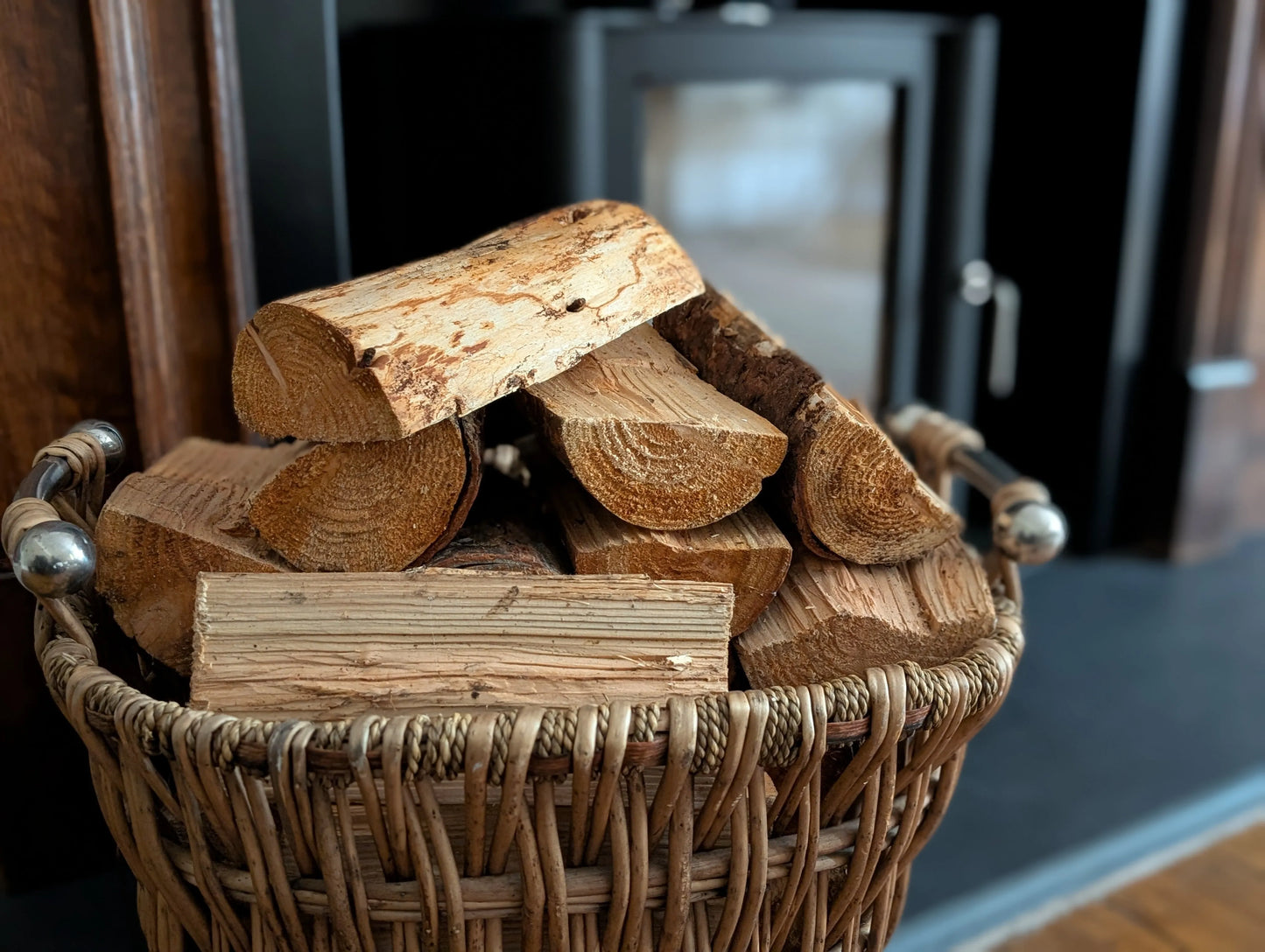 Kiln Dried British Wood Burner Logs in a wicker basket by fireplace.
